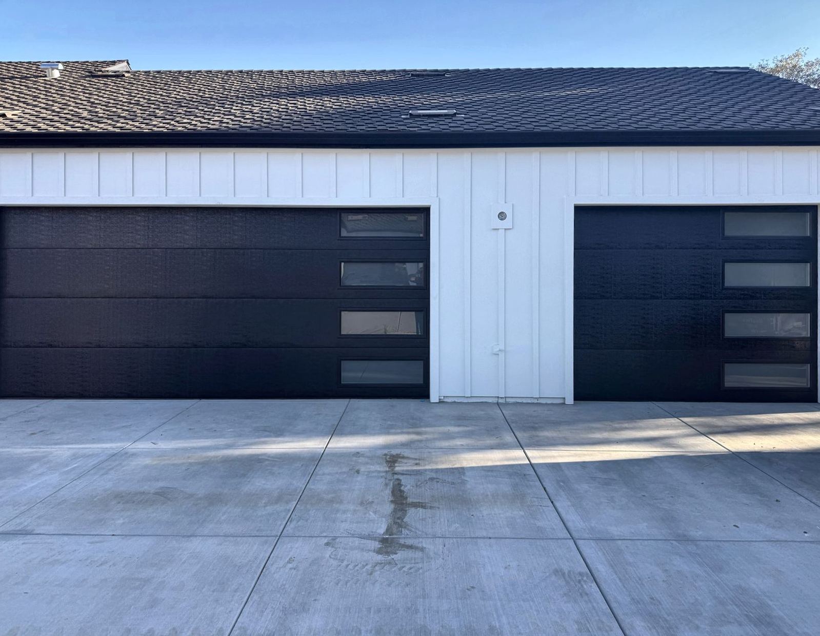 Two black modern garage doors on a white garage