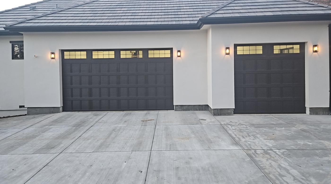 Two black 4-layer garage doors with grid windows at dusk