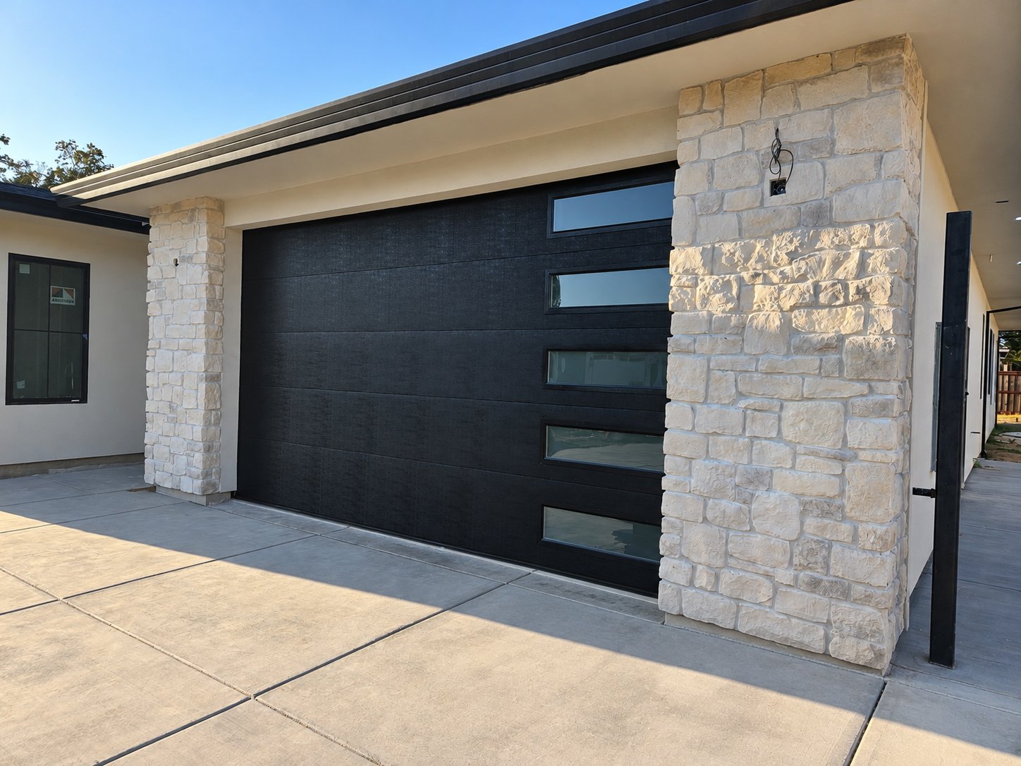 Black flush garage door with side windows between stone columns