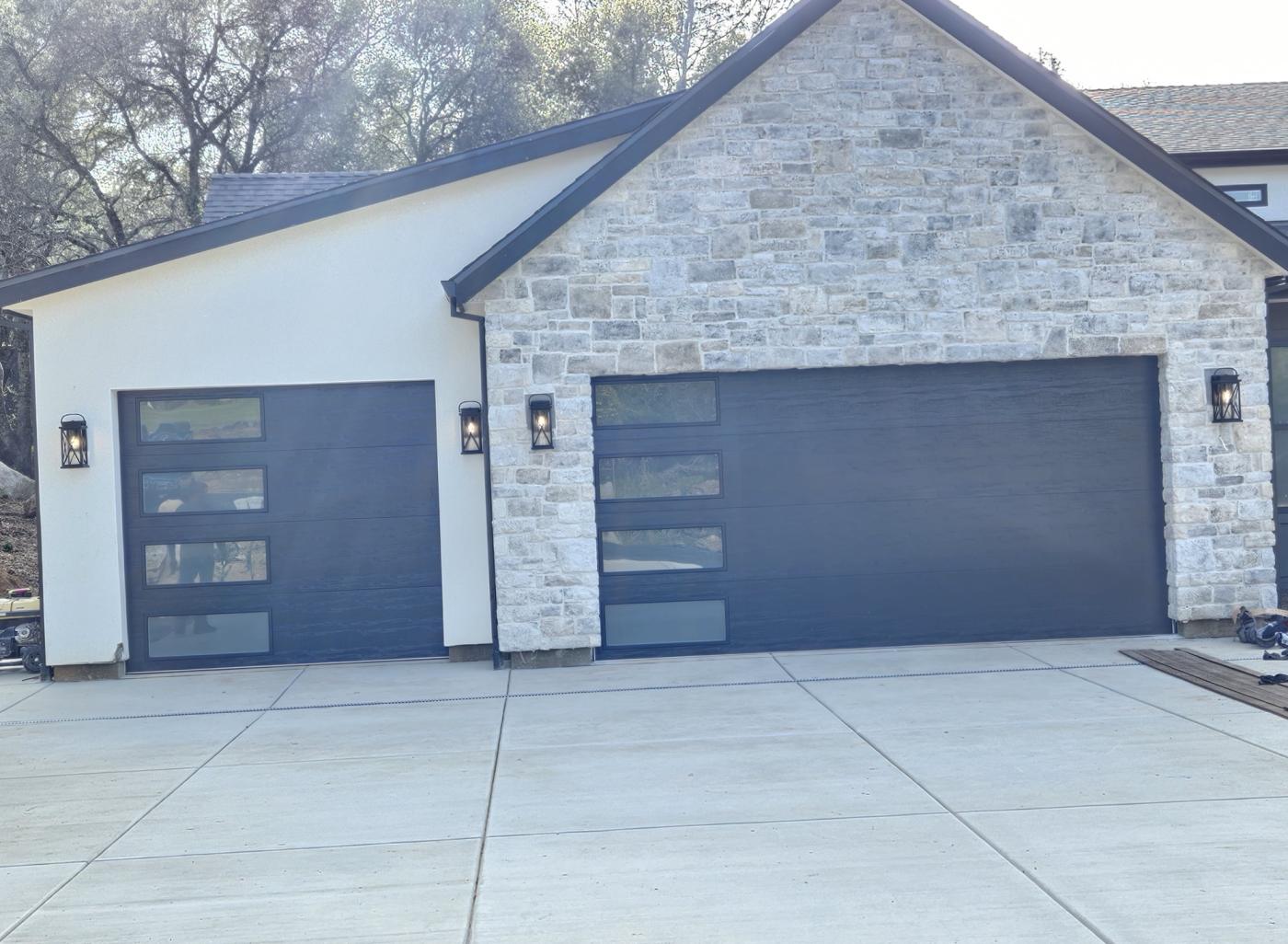 Two black flush garage doors with side windows on a stone home